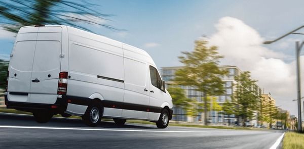 En vit skåpbil kör snabbt genom en stad för effektiv paketleverans.
